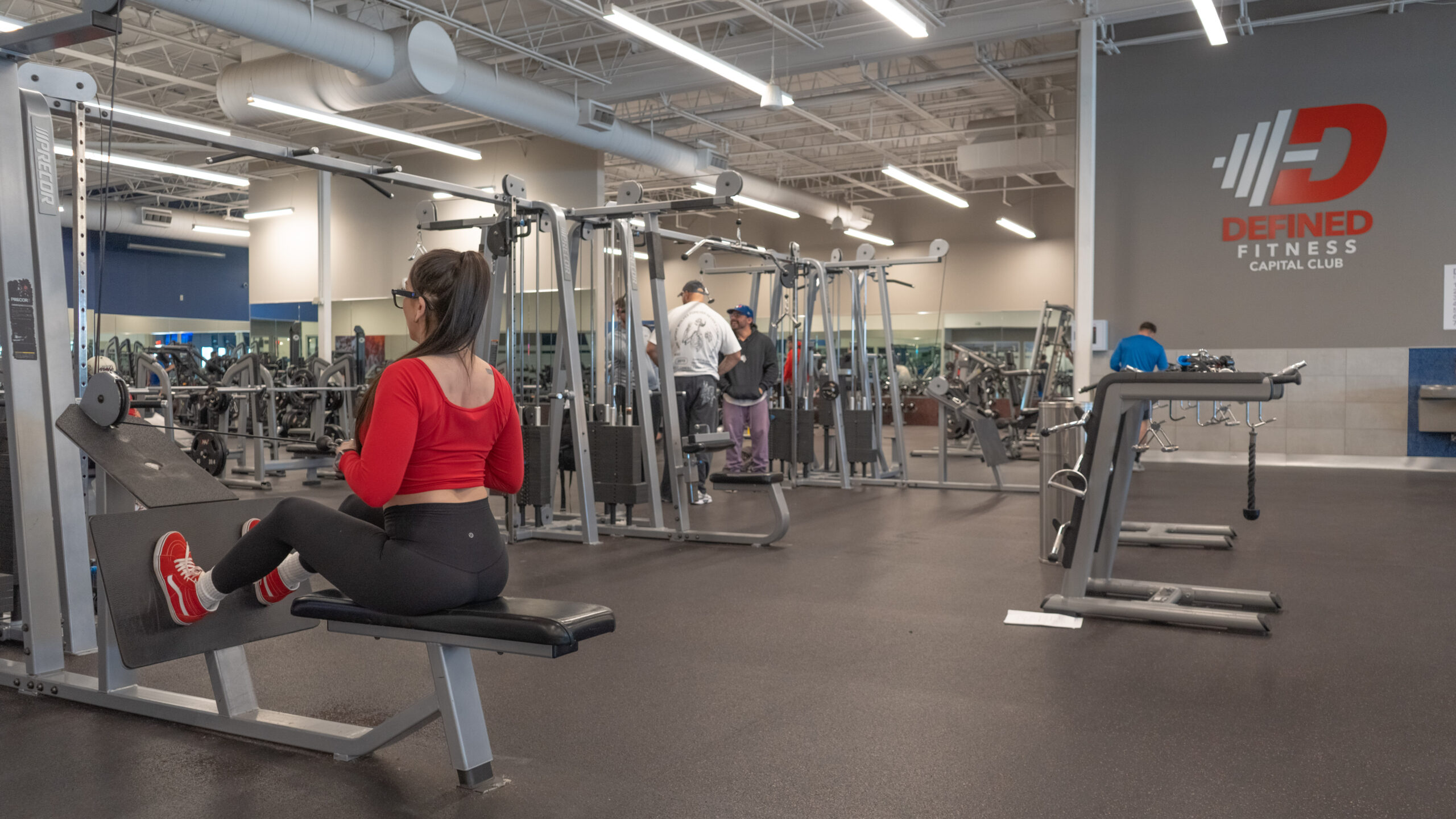 Woman seated at a cable row machine at Defined Fitness Capital Club, positioned at the start of the movement with arms extended toward the cable attachment.